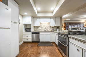 Kitchen featuring sink, dark hardwood / wood-style floors, appliances with stainless steel finishes, tasteful backsplash, and white cabinetry