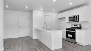 Kitchen with appliances with stainless steel finishes, light hardwood / wood-style flooring, white cabinetry, and sink