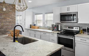 Kitchen with white cabinetry, sink, stainless steel appliances, plenty of natural light, and decorative light fixtures