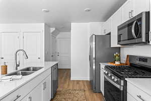 Kitchen with a textured ceiling, stainless steel appliances, sink, hardwood / wood-style flooring, and white cabinets