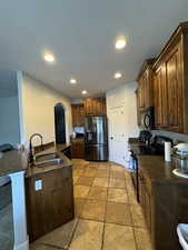 Kitchen with black appliances, dark stone countertops, kitchen peninsula, and sink