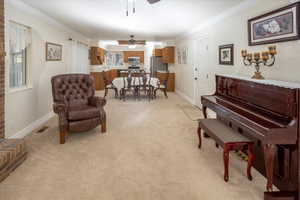 Living area with ceiling fan, light carpet, and ornamental molding