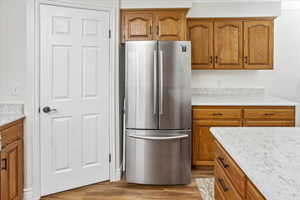 Kitchen with stainless steel fridge, light stone countertops, and light wood-type flooring