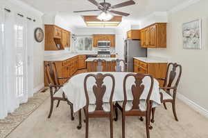 Dining room with light carpet, ceiling fan, ornamental molding, and sink