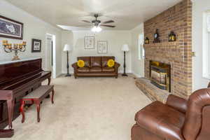 Living room featuring light carpet, a brick fireplace, a textured ceiling, ceiling fan, and crown molding