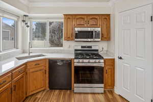 Kitchen featuring appliances with stainless steel finishes, ornamental molding, sink, pendant lighting, and light hardwood / wood-style floors