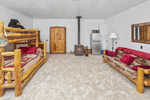 Bedroom with a wood stove, stainless steel fridge, carpet, and a textured ceiling