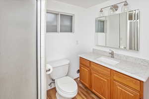 Bathroom featuring a shower with door, vanity, wood-type flooring, and toilet