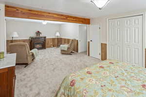 Carpeted bedroom with a fireplace, beam ceiling, a closet, and wooden walls