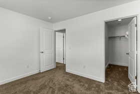 Unfurnished bedroom featuring a walk in closet, dark carpet, and a closet