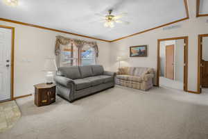 Carpeted living room featuring vaulted ceiling, ceiling fan, and crown molding