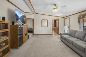 Living room featuring ceiling fan, light colored carpet, lofted ceiling, and ornamental molding