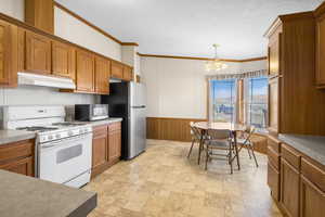 Kitchen featuring pendant lighting, ornamental molding, a textured ceiling, appliances with stainless steel finishes, and a chandelier