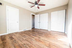 Unfurnished bedroom featuring light wood-type flooring, ceiling fan, and multiple closets