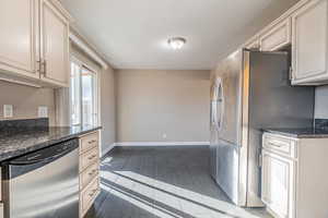 Kitchen featuring dark stone countertops, light tile patterned floors, cream cabinetry, and appliances with stainless steel finishes