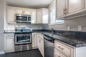 Kitchen with sink, stainless steel appliances, and dark stone counters