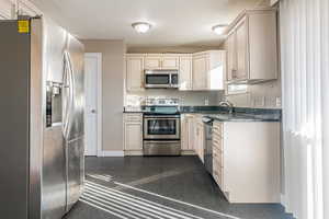 Kitchen with cream cabinetry, stainless steel appliances, dark stone countertops, and sink