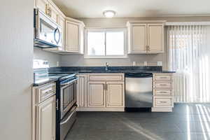 Kitchen with sink, stainless steel appliances, cream cabinets, plenty of natural light, and dark stone counters