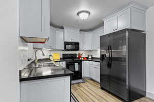 Kitchen with a textured ceiling, sink, black appliances, light hardwood / wood-style flooring, and white cabinets