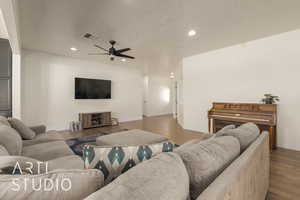 Living room with ceiling fan, wood-type flooring, and a textured ceiling