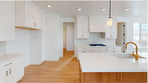 Kitchen with pendant lighting, white cabinets, a sink, black gas stovetop, and premium range hood