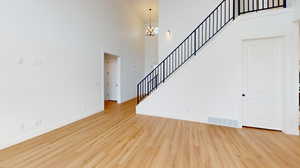 Unfurnished living room featuring an inviting chandelier, baseboards, visible vents, and wood finished floors