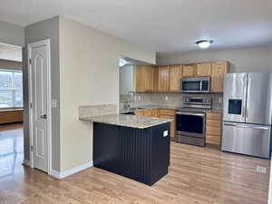 Kitchen with kitchen peninsula, appliances with stainless steel finishes, tasteful backsplash, sink, and light hardwood / wood-style floors