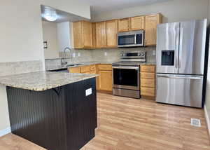 Kitchen with kitchen peninsula, sink, light hardwood / wood-style flooring, and appliances with stainless steel finishes