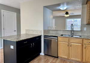 Kitchen with dishwasher, light stone countertops, kitchen peninsula, and sink