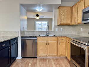 Kitchen featuring light stone countertops, sink, light wood-type flooring, and appliances with stainless steel finishes