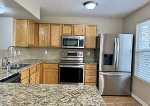 Kitchen with backsplash, sink, light stone countertops, and stainless steel appliances