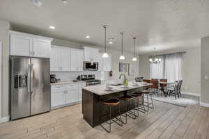 Kitchen with white cabinetry, pendant lighting, an island with sink, and stainless steel appliances