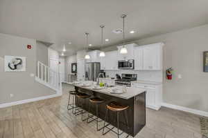 Kitchen featuring a kitchen bar, white cabinets, an island with sink, and appliances with stainless steel finishes