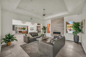 Living room with a raised ceiling, a fireplace, light tile patterned floors, and plenty of natural light