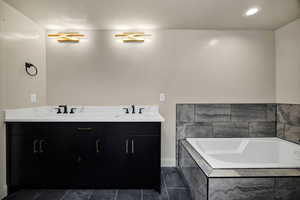 Basement Bathroom in primary suite 2 with double vanity, a bath, dark tile patterned flooring, and recessed lighting