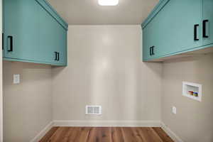 Laundry area with cabinet space, wood finished floors, hookup for a washing machine, and a textured ceiling