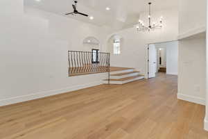 Unfurnished living room featuring ceiling fan with notable chandelier, light wood-type flooring, and a towering ceiling