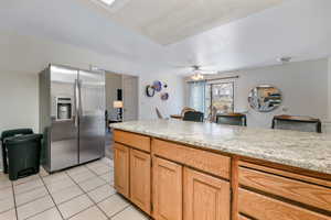 Kitchen featuring ceiling fan, light stone counters, stainless steel fridge with ice dispenser, and light tile patterned floors