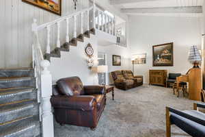 Carpeted living room featuring beamed ceiling, high vaulted ceiling, and wooden walls