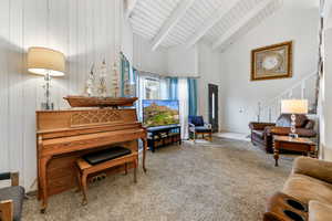 Interior space featuring carpet flooring, wood walls, beamed ceiling, and high vaulted ceiling