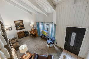 Living room with lofted ceiling with beams, wooden walls, wood ceiling, and light carpet