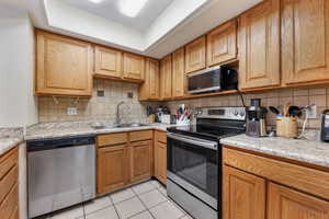 Kitchen featuring decorative backsplash, appliances with stainless steel finishes, light stone counters, sink, and light tile patterned floors