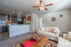 Living room with a textured ceiling, dark carpet, and ceiling fan