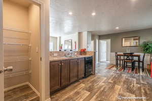 Kitchen featuring hardwood / wood-style floors, sink, a textured ceiling, dark brown cabinets, and beverage cooler