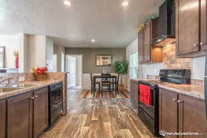 Kitchen with sink, wall chimney range hood, dark hardwood / wood-style flooring, a textured ceiling, and black appliances