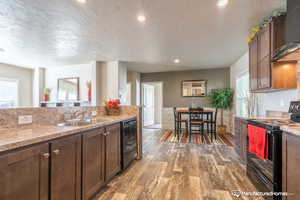 Kitchen with a textured ceiling, wall chimney range hood, sink, black appliances, and hardwood / wood-style floors