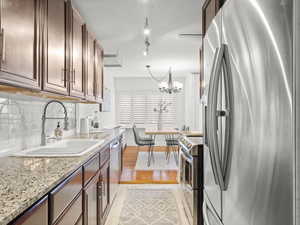 Kitchen with light stone counters, stainless steel appliances, sink, pendant lighting, and a chandelier