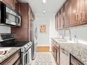 Kitchen featuring light stone countertops, sink, stainless steel appliances, tasteful backsplash, and track lighting