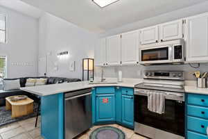 Kitchen featuring appliances with stainless steel finishes, blue cabinets, sink, white cabinets, and plenty of natural light