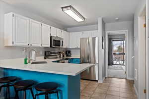 Kitchen featuring white cabinets, sink, light tile patterned floors, and stainless steel appliances